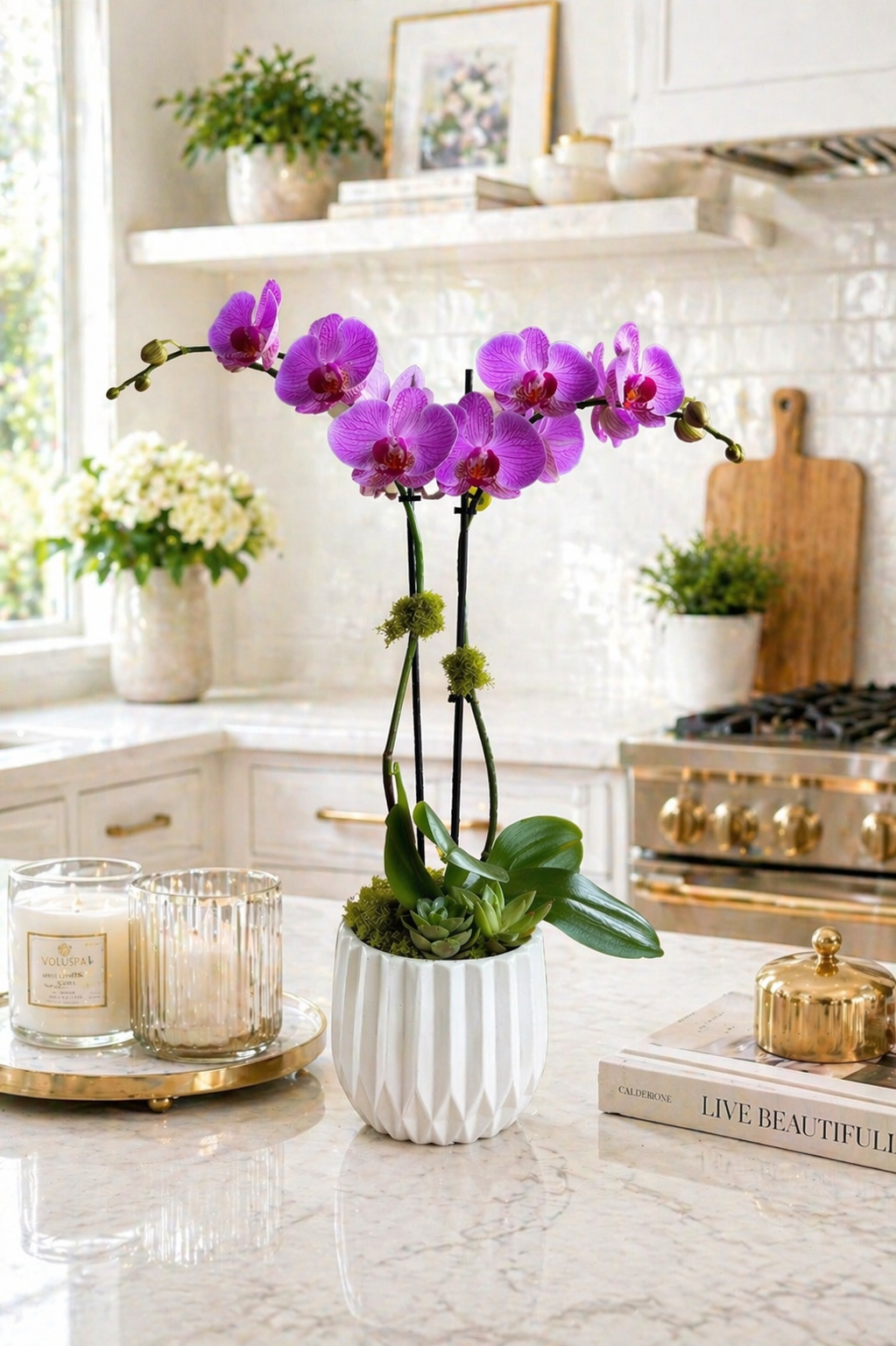 Purple orchid in a white pot on a kitchen counter with candles and decor.