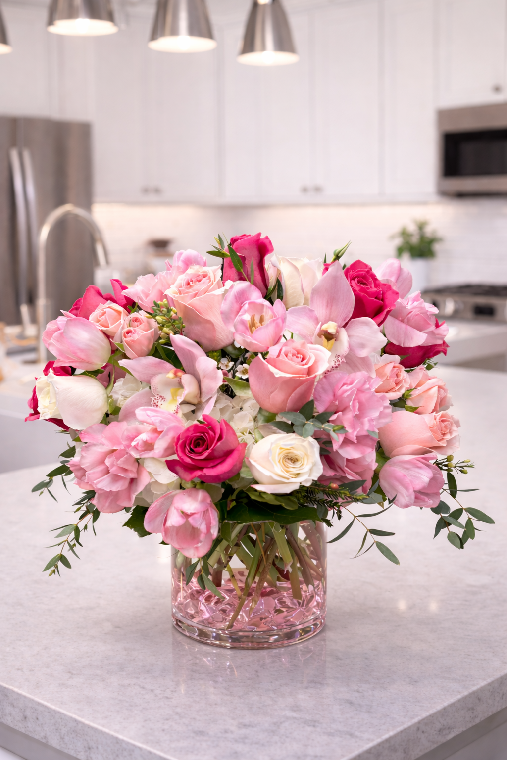 Bouquet of pink and white flowers in a clear vase on a kitchen counter.