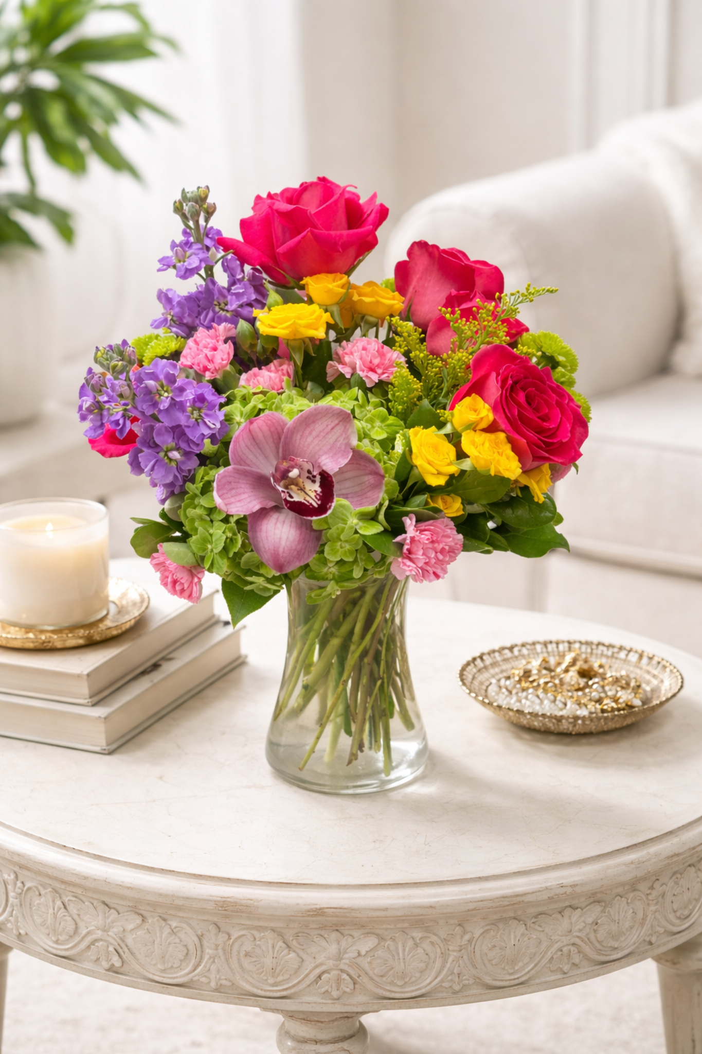 Colorful bouquet of flowers in a glass vase on a decorative table with a candle and books.