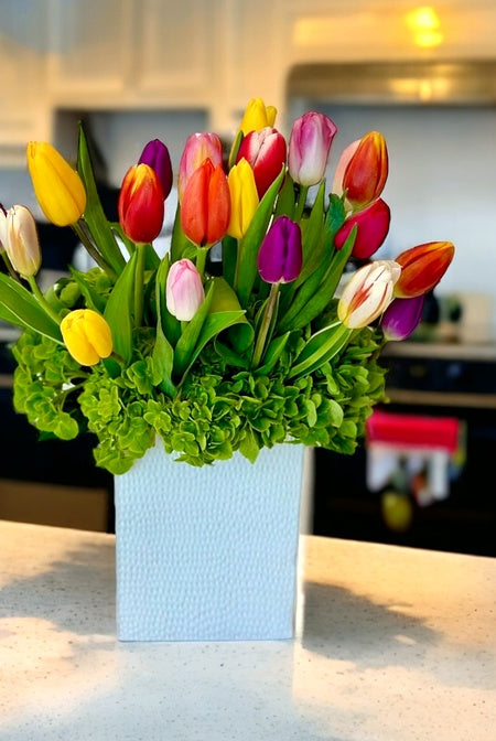 Colorful tulips in a light blue vase on a kitchen counter